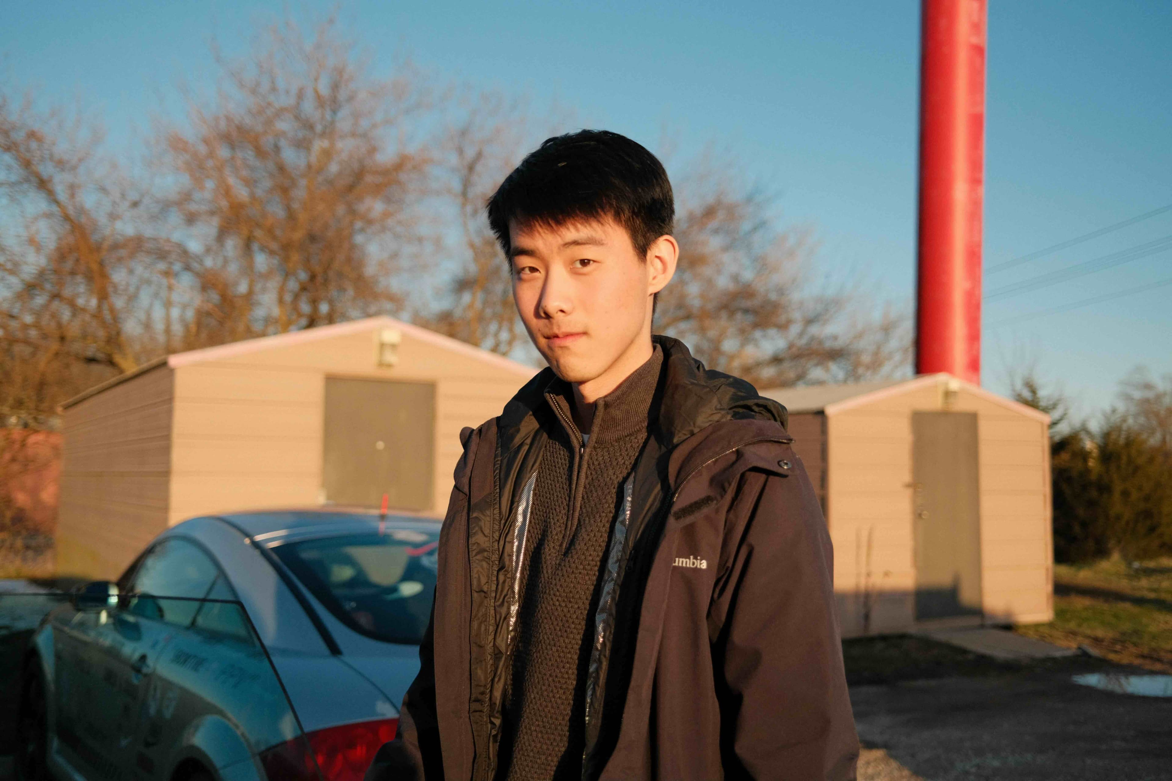 Picture of Albon wearing a coat with two sheds in the background.